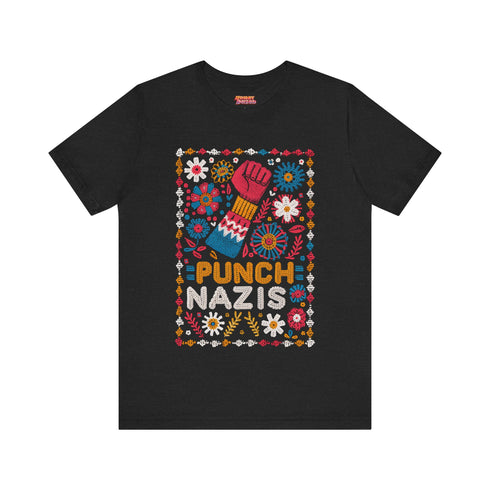 Black t-shirt featuring an embroidered-style design with the phrase "PUNCH NAZIS" in bold, colorful lettering. Above the text, a raised red fist is illustrated, symbolizing resistance, and is surrounded by a vibrant folk-art-inspired floral border with bright flowers, leaves, and geometric patterns in red, yellow, blue, and white.